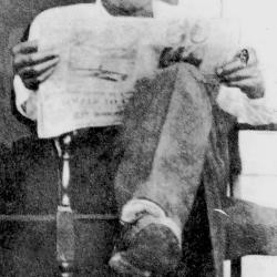 David W. Richardson sitting on porch in chair reading a newspaper